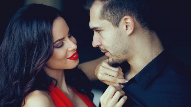 Woman in red dress touching man in black shirt while looking at each other.